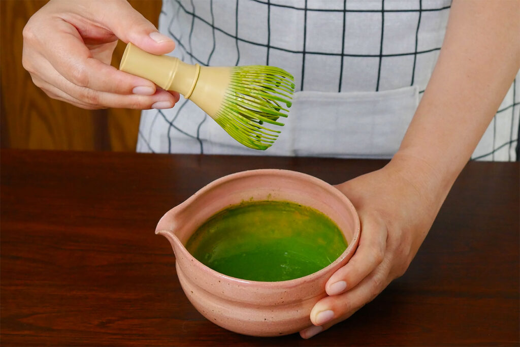 Matcha Tee aufschlagen mit einem Bambusbesen.